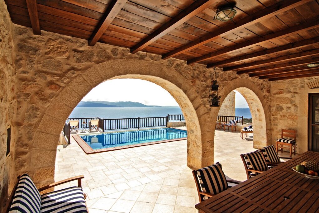 The covered veranda's stone arches opening onto the pool terrace and the wide bay below