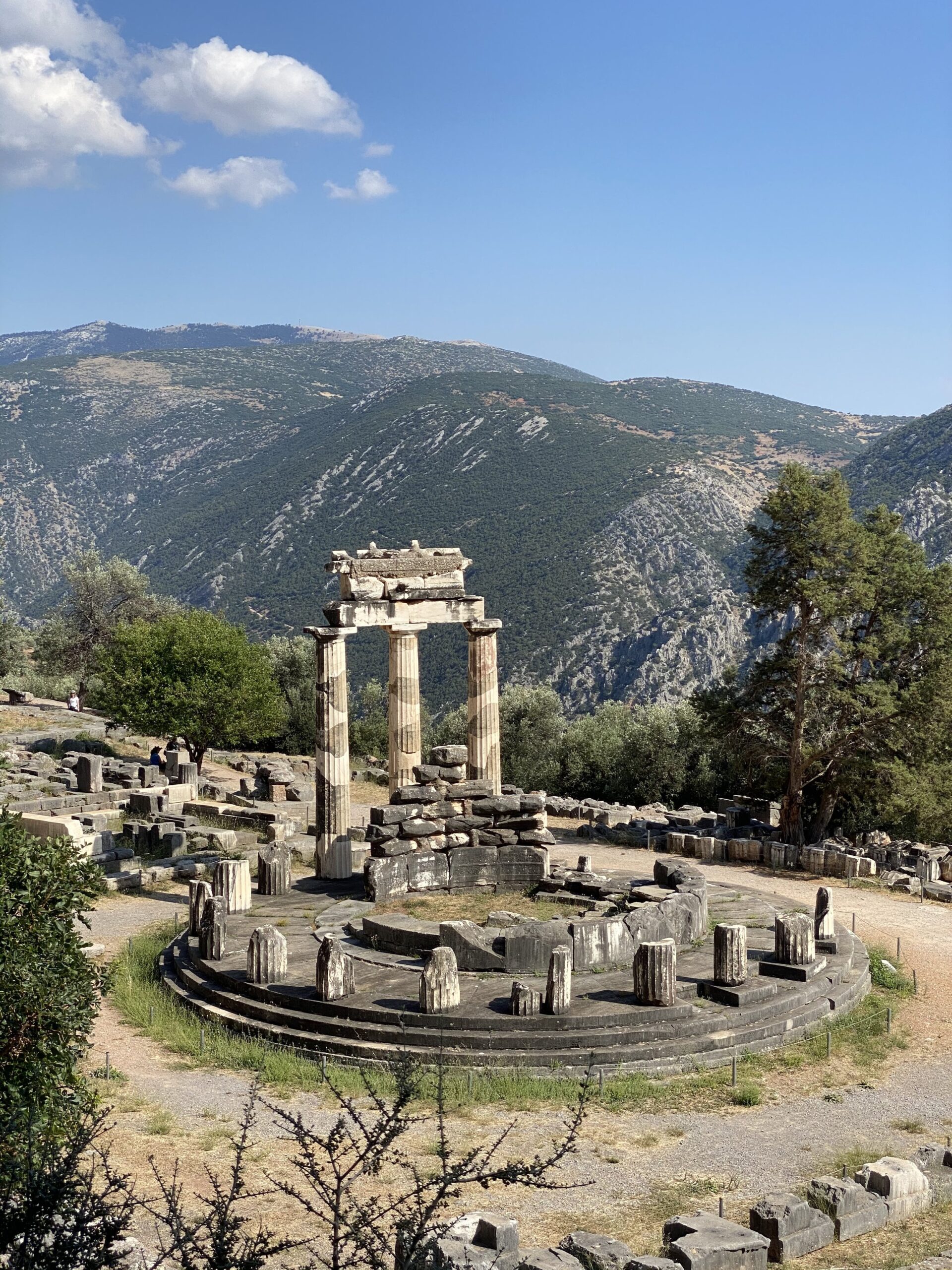 The round tholos of Delphi standing among the ruins of the sanctuary, mountain slopes rising behind