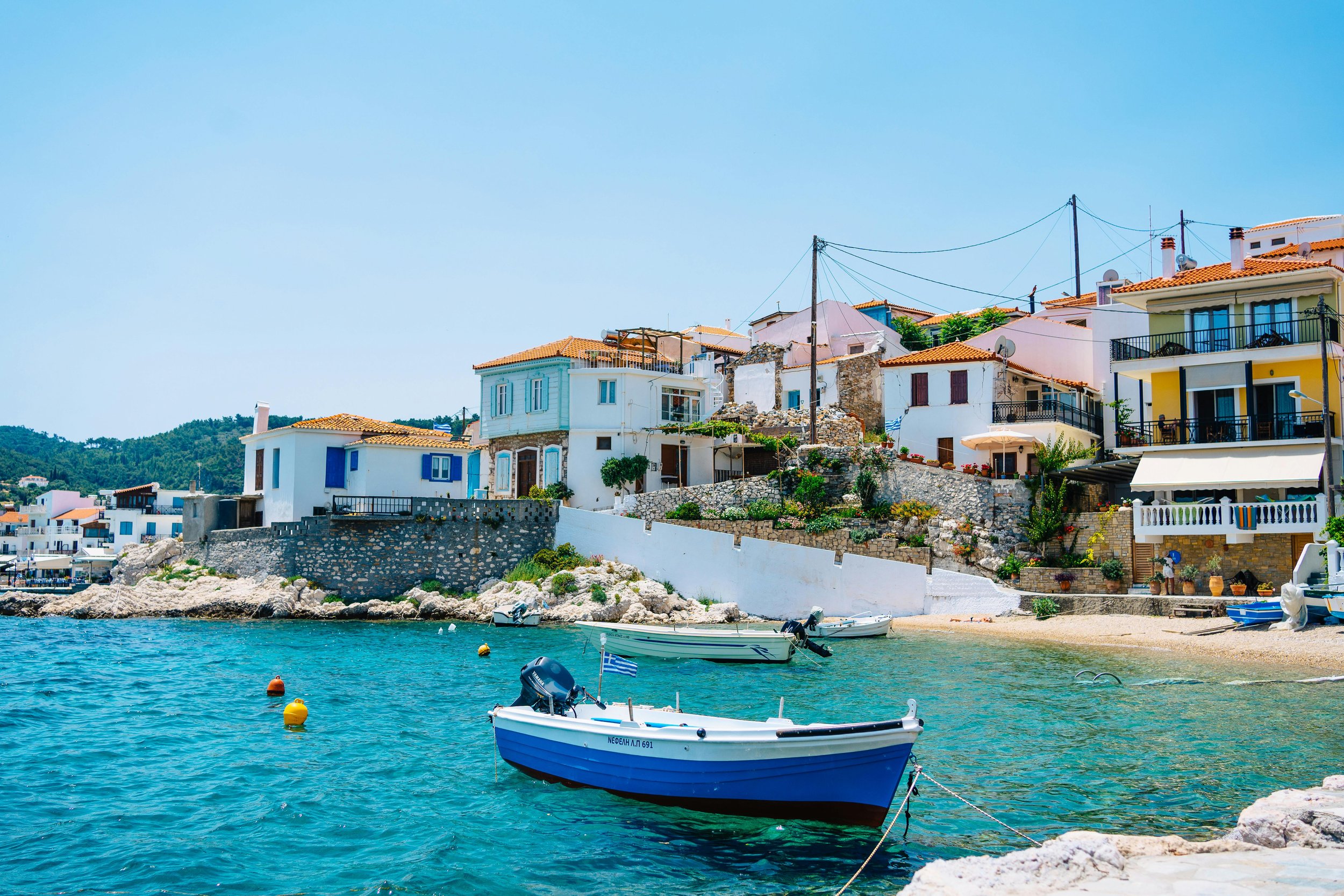 Blue-and-white fishing boats moored in the clear shallows of a Greek harbourside village